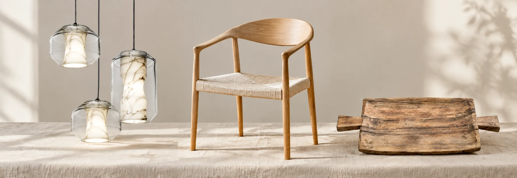 Lámparas colgantes de vidrio, silla de roble y bandeja de madera sobre lino.